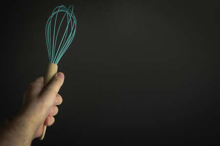 Hand holding whisk on black backgroundの写真素材