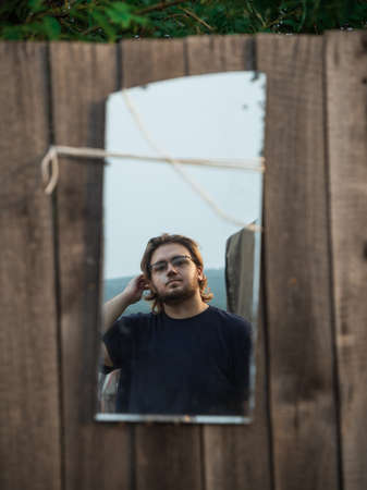 Portrait of a young man in the mirror on a wooden fenceの写真素材
