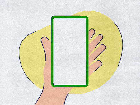 Hand holding a phone on a yellow paper backgroundの写真素材