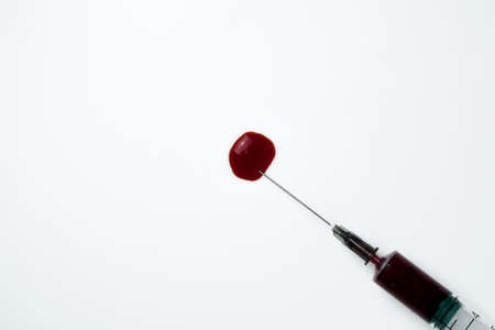 Medical syringe and needle with a drop of blood on a light backgroundの写真素材