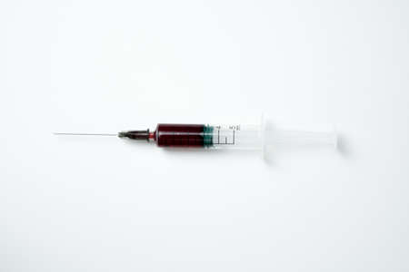 Medical syringe and needle with red blood on a light backgroundの写真素材