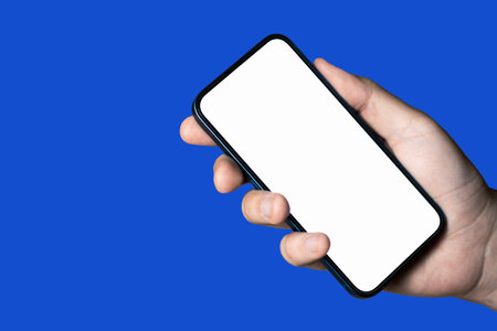 Hand holding a phone with empty white screen on blue backgroundの写真素材