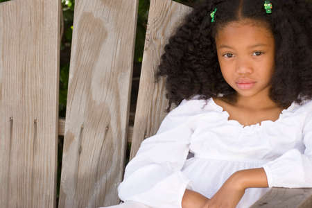 Happy African American little girl sitting on a bench.の写真素材