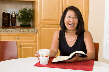 Asian woman reading at her kitchen table.