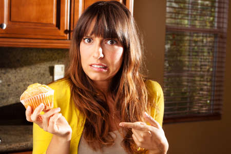 Young woman concerned about eating a cupcake.の写真素材