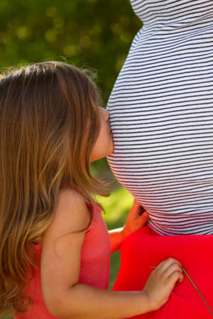 Little girl kissing her pregnant mothers belly.