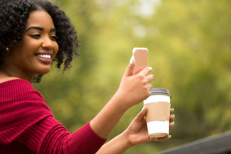 African American Woman texting and drinking coffee.