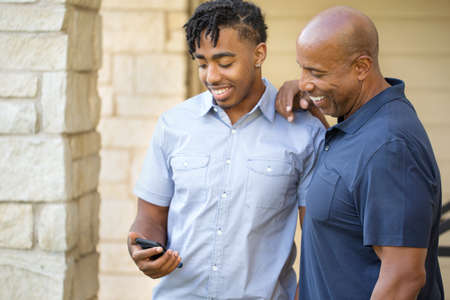 African American father and his adult son texting.の写真素材