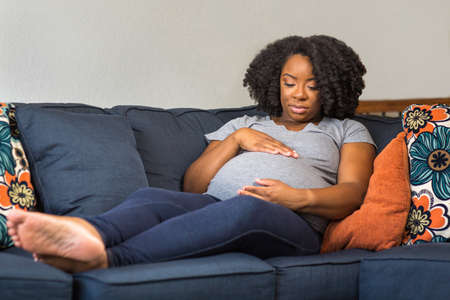 African American Pregnant Woman Sitting On A Sofa