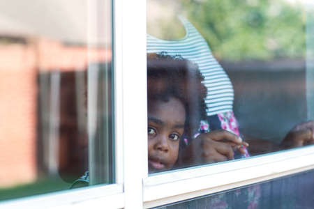 Young African American little girl looking out the window.の写真素材