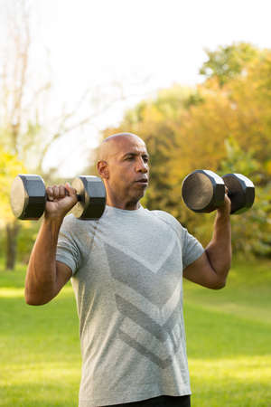 Fit African American man lifting weights outside.