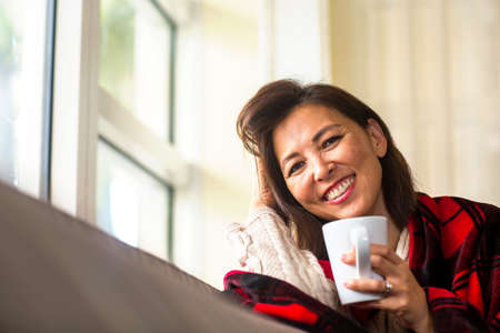 Mature Asian woman enjoying a cup of coffee.の写真素材