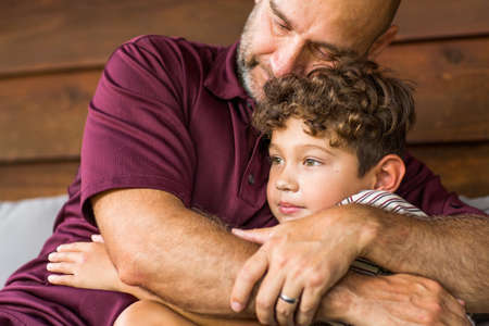 Hispanic father sitting and hugging his son.の写真素材