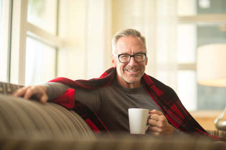 Mature man sitting on a sofa drinking coffee.の写真素材