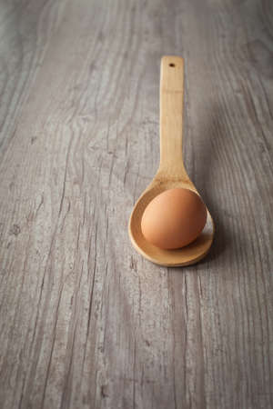 Raw egg on a wooden spoon on the table