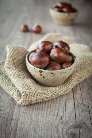 Bunch of fresh chestnuts in a bowl on wooden tableの写真素材