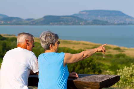 Elderly couple sitting at the lakeside benchの写真素材
