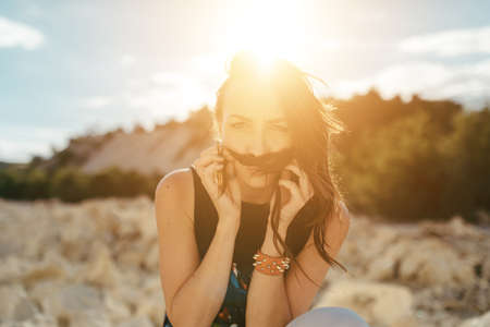 Young woman posing near the beautiful mountains dressed colorful clothes sitting on a stoneの写真素材