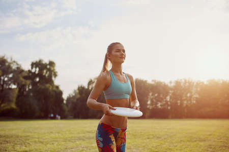 Young athletic girl playing with flying disc in the park. Professional player. Sport concept. Ultimate. Focus on flying discの写真素材