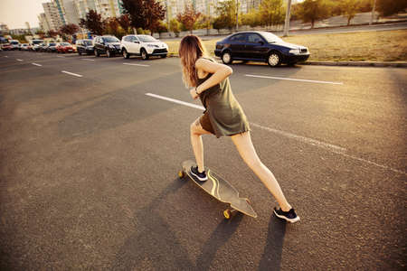 Beautiful young girl with tattoos riding on his longboard on the road in the city in sunny weather. Extreme sportsの写真素材