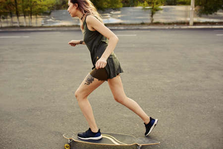 Beautiful young girl with tattoos riding on his longboard on the road in the city in sunny weather. Extreme sportsの写真素材