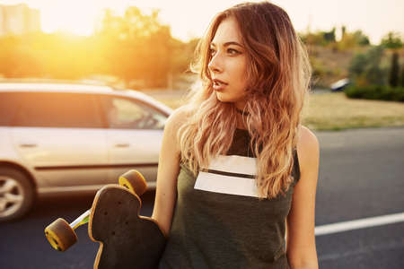 Beautiful young tattooed woman with his longboard on the road in the city in sunny weatherの写真素材