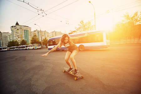 Beautiful young girl with tattoos riding on his longboard on the road in the city in sunny weather. Extreme sportsの写真素材