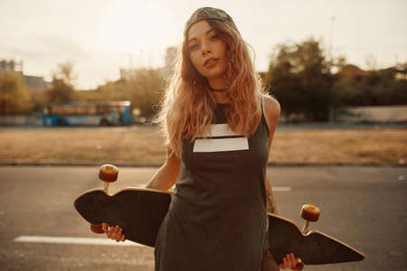 Beautiful young tattooed woman with his longboard on the road in the city in sunny weatherの写真素材