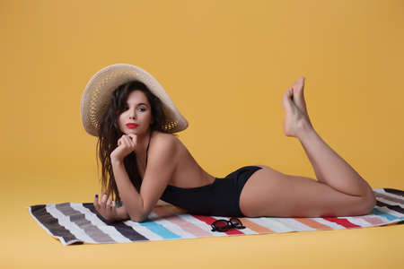 Fashion photo of beautiful and young lady in swimsuits posing in studio, is resting on a colorful...