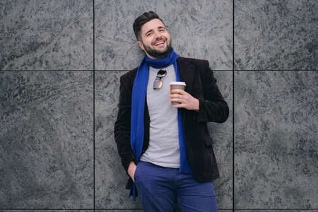 Handsome young man wearing sunglasses on a walk in town. Dreamful guy is relaxing with hot drinkの写真素材