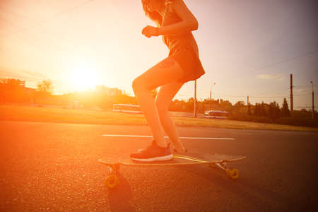 Beautiful young girl with tattoos riding on his longboard on the road in the city in sunny weather. Extreme sportsの写真素材