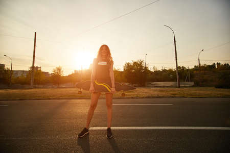 Beautiful young girl with tattoos riding on his longboard on the road in the city in sunny weather. Extreme sportsの写真素材