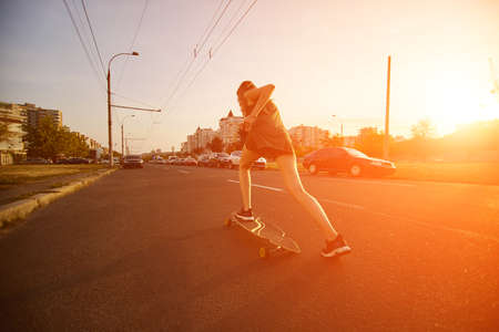 Beautiful young girl with tattoos riding on his longboard on the road in the city in sunny weather. Extreme sportsの写真素材