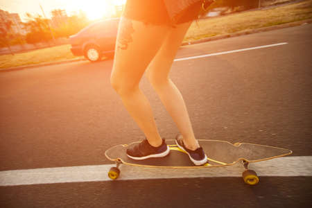Beautiful young girl with tattoos riding on his longboard on the road in the city in sunny weather. Extreme sportsの写真素材