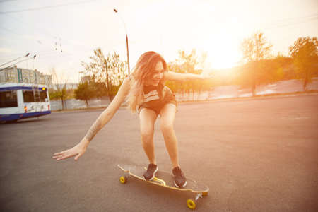 Beautiful young girl with tattoos riding on his longboard on the road in the city in sunny weather. Extreme sportsの写真素材