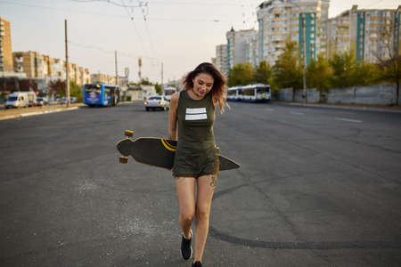 Beautiful young tattooed woman with his longboard on the road in the city in sunny weatherの写真素材
