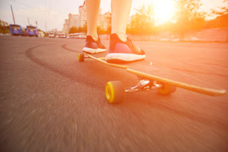 Beautiful young girl with tattoos riding on his longboard on the road in the city in sunny weather....