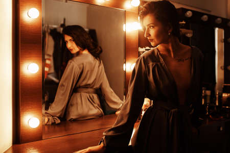 Beautiful sexy girl near the mirror in the dressing room in a gray silk dressing gown