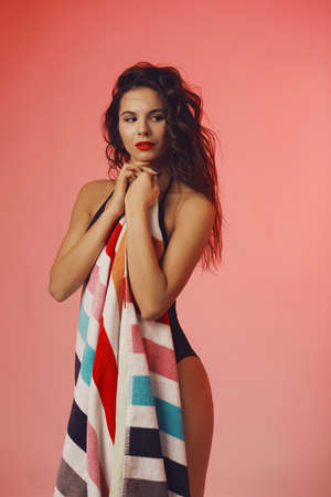 Sexy attractive brunette woman posing in black fashionable swimsuit in studio holding colorful towelの写真素材