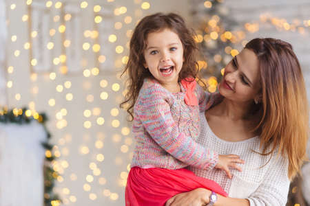 Happy loving family. Mother and her daughter girl play at home in Christmas lights. Funny mom and lovely child having fun indoors.の写真素材