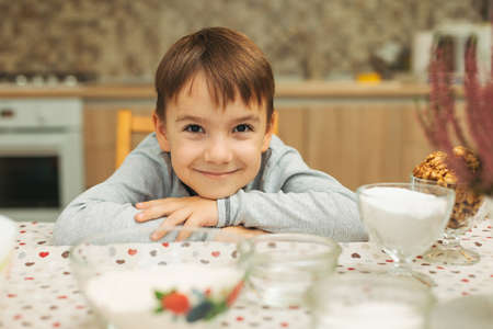 Portrait smiling cute boy looking to camera in warm house atmosphere, sitting at the kitchen tableの写真素材