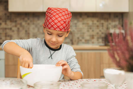Boy is cooking in a luminous kitchen mixing the preparation while anticipating how tasty it will be.の写真素材