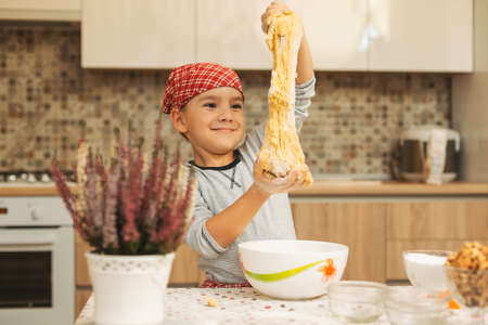 Cheerful boy making dough for biscuits. Child making cookies using baking molds for Christmas Holidays in the kitchen. Kid holding dough in hands smiling in the kitchen.の写真素材