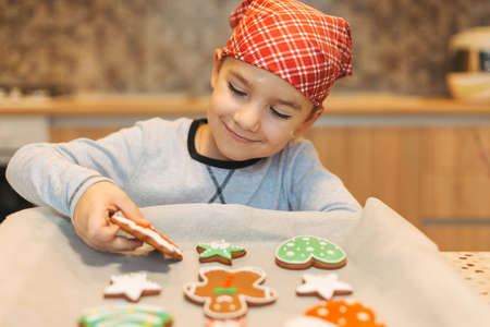 Happy boy anticipating how tasty are fresh baked Christmas biscuits holding one in hand. Cute boy chef enjoying perfect taste of fresh baked Christmas cookies.の写真素材