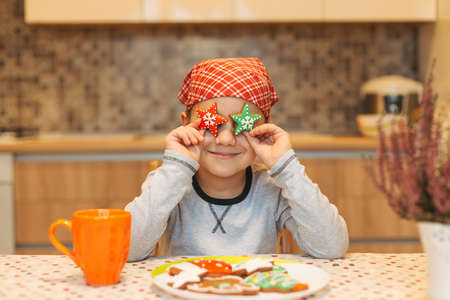 Funny boy having fun at home, holds cookies stars before his eyes like in glasses smiling, showing tongue, while cooking in the kitchen.の写真素材