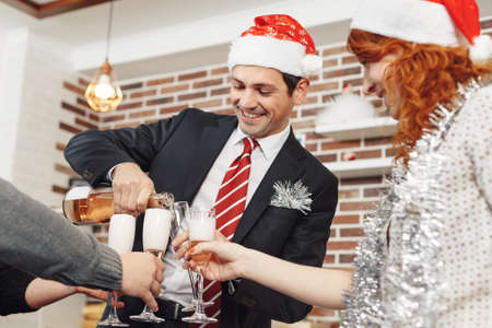 Happy businessman in Santa cap pouring champagne into his colleagues glasses in office. Merry Christmas and Happy New Year 2018の写真素材