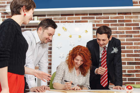 Corporate Christmas celebration in the office. Co-workers having fun at Christmas day, writing a...