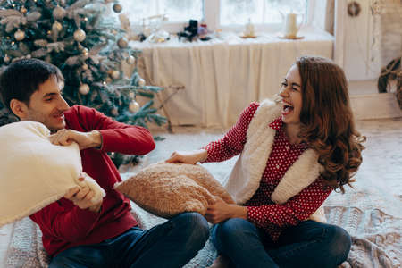 Happy loving caucasian couple is getting crazy on the Christmas eve near the New Year tree, they are...