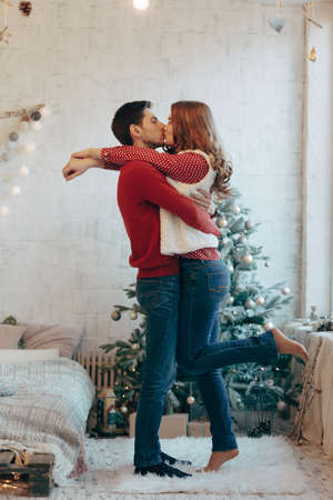 Picture showing young couple hugging and kissing over Christmas tree, full lengthの写真素材