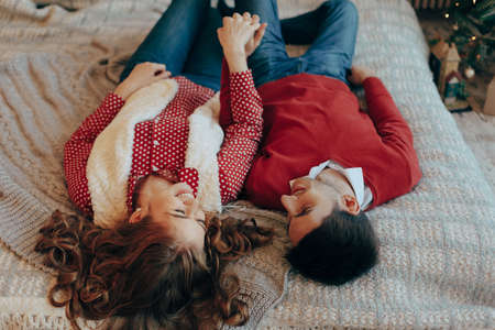 Young attractive couple lays on the bed, looking to each other spending time together. Top view. Young couple laying on the bed smiling with heads upside down.の写真素材